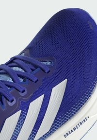 Athletic sneaker in royal blue knit material, featuring silver three-stripe design and textured lacing system. "DREAMSTRIKE+" on sole.
