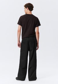 Pantalones negros de pierna ancha con una textura suave, que cuentan con dos bolsillos traseros y un diseño minimalista, combinados con una camiseta oscura de manga corta.