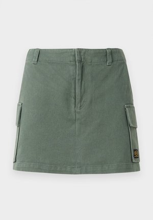 Grön denimkjol med en åtsittande midjeband, två sidofickor och en applikation på nedre höger sida. Slät textur med en subtil lyster.