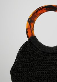 Zwarte gehaakte tas met grote ronde handvatten van plastic in schildkleur op een neutrale achtergrond.