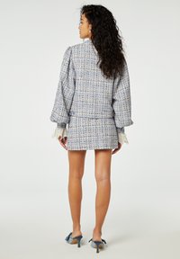 Tweedjack en rok set in lichtblauw met veelkleurige draden, met pofmouwen en kantaccenten bij de manchetten.