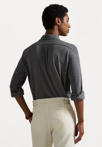 Šedá polo košile s dlouhým rukávem a ohrnutým límcem, s ohrnutými rukávy a jemnou texturou, spárovaná se světle barevnými kalhotami.