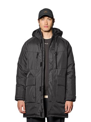 Mann trägt einen schwarzen Wintermantel mit Kapuze, Frontreißverschluss und großen Taschen, kombiniert mit einer schwarzen Baseballkappe und dunkler Kleidung darunter.