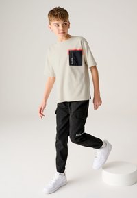 Heledast beežist l�ühikeste varrukatega t-särk punase ja musta rahakotiga; mustade cargo-pükste ja valgete tossudega, millel on logode aktsendid.