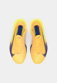 Ryškiai geltonos sportinės bateliai su purpuriniais ir juodais akcentais, turintys lengvą tinklinį viršų, plokščias raišteles ir paminkštintą sole.