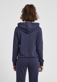 Mörkblå hoodie av mjukt tyg, med en avslappnad passform, långa ärmar och en stor huva, samt ribbade muddar och nederkant.