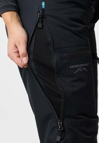 Zwarte outdoorbroeken met een halfopen rits, die een netvoering onthult. Voorzien van een "SWEDEMOUNT" logo en een klein accent van de Zweedse vlag.