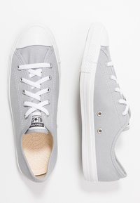 Szare kanvasowe trampki z białym gumowym noskiem i podeszwą, z płaskimi białymi sznurówkami i metalowymi oczkami, z teksturowaną wkładką.