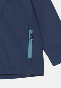 Navy waterproof jacket featuring a contrasting light blue zip pocket and texture, with a straight hem and adjustable elements at the bottom.