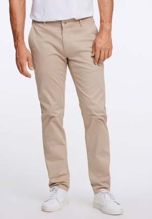 Beige chino's met een slim fit, gemaakt van katoen. Voorzien van een ritsgulp, voorzakken en een gladde textuur. Gemaakt in combinatie met witte sneakers.