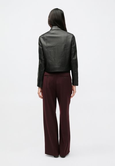 Čierna kožená skrátená bunda a tmavohnedé široké nohavice. Hladká textúra s jednoduchými stehovými detailmi. Sako strihané na mieru okolo pásu.