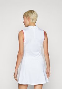 Vit ärmlös klänning med pikékrage, med r�öda detaljer längs axlarna och en dragkedja bak. Slät, elastisk tyg.