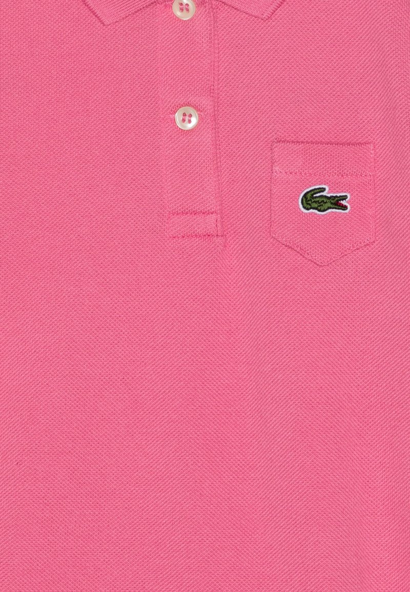 Polo shirt en coton rose avec un tissage texturé, col à trois boutons et un petit logo crocodile vert sur la poche poitrine.