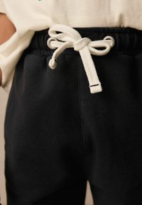 Schwarze Sweatpants mit einem Kordelzug in der Taille, die ein weißes Band und Metallösen aufweisen. Der Stoff ist weich und strukturiert, ideal für lässige Outfits.