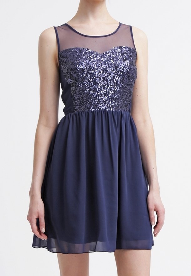 Femme portant une robe bleu marine sans manches avec un corsage en sequins et un décolleté transparent, debout les bras détendus le long du corps.