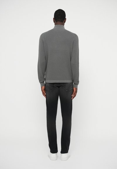 Gray knit pullover with a high collar, paired with black jeans. Model wears white sneakers, minimalistic design with clean lines.
