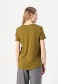 Kortärmad, olivgrön t-shirt med rund halsringning. Mjukt bomullstyg, något figursydd design. Bärs med ljusgrå vida byxor.