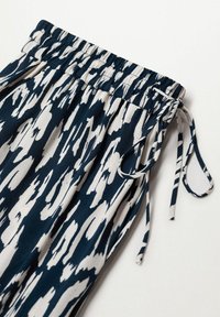 Tissu bleu marine et beige à motifs avec une taille élastique, des lien de serrage, et une texture lisse, présentant un design abstrait.