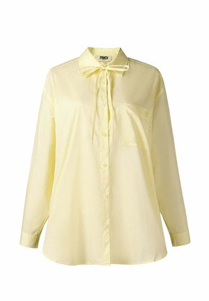 Lichtgele blouse met lange mouwen, knoopsluiting aan de voorkant, borstzak, kraag en een gestrikte strik bij de hals, afgebeeld op een witte achtergrond.