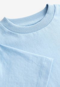 Lyseblå t-shirt med ribbet rund hals, korte ærmer, glat tekstur og subtile sy-detaljer ved kanten og ærmerne.