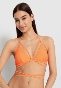 Oranssi bikinitoppi, jossa on kolmiomainen muotoilu ja useita hihnatietoja, jotka luovat ristikkäisen vaikutelman. Valmistettu sileästä, venyvästä kankaasta.