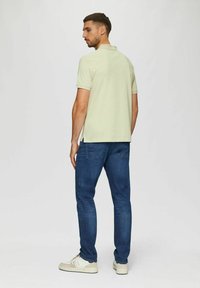 Hellgrünes Polohemd mit kurzen Ärmeln, kombiniert mit dunkelblauen Jeans und weißen Sneakers. Das Hemd hat Seitenschlitze für zusätzlichen Komfort.