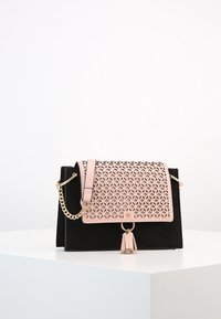 Svart sametsväska med ett rosa laserutskuret geometriskt lock, guld kedjerem och tofsdetalj. Kompakt design, strukturerad form.