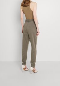 Khaki trousers with a high waist, belt, side pockets, and tapered legs paired with cream heeled shoes and a tan sleeveless top.