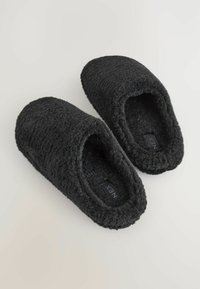 Saboti negri, din material moale, cu vârf rotunjit și spate deschis. Exterior texturat și interior pufos pentru confort. Eticheta brandului vizibilă în interior.