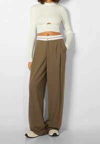 Bílý žebrovaný krátký rukáv top s výřezem, v kombinaci s volnými hnědými širokými kalhotami a světlými teniskami.