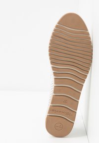 Semelle d'une chaussure blanche avec une semelle extérieure en caoutchouc beige présentant des rainures ondulées, taille 37, et logo de la marque embossé au niveau du talon.