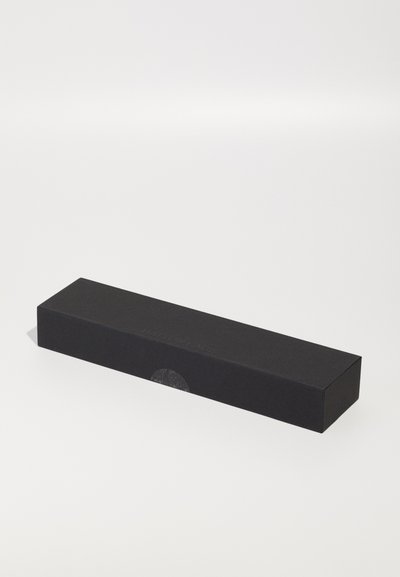 Boîte rectangulaire noire en papier mat, avec un branding en relief sur le côté et un détail en forme de découpe circulaire à une extrémité.