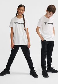 Hvide bomulds t-shirts med sort "hummel" logo, parret med sorte joggingbukser. Modellerne har sorte sneakers på. En enkel, afslappet sportswear stil.