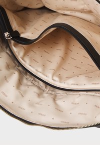 Schwarze Handtasche mit einem beigen Stofffutter, das dezente Drucklogos und kleine dreieckige Muster aufweist. Mit Reißverschlussfächern ausgestattet.
