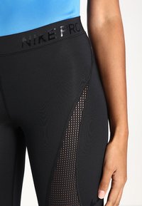 Legginsy Nike Pro wykonane z czarnego materiału z siateczkowymi wstawkami, z solidnym pasem w talii z odblaskowym logo oraz dopasowanym krojem.