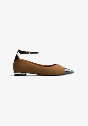 Ballerines en suede marron avec un bout pointu en vernis noir et une lanière à la cheville. Présentent un petit accent métallique sur le talon.