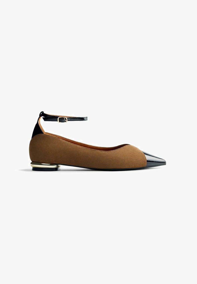 Ballerines en suede marron avec un bout pointu en vernis noir et une lanière à la cheville. Présentent un petit accent métallique sur le talon.