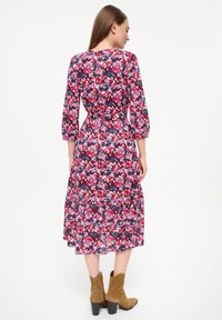 Kvetinové mididress v tmavomodrej farbe, s ružovými a bielymi kvetmi, dlhým rukávom, priliehajúcim pásom a poschodovou sukňou, v kombinácii s hnedými členkovými čižmami.