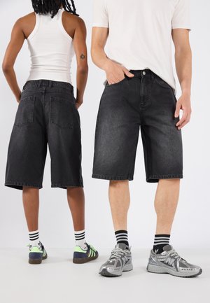 Shorts de mezclilla negra con un corte holgado, que cuentan con cinco bolsillos. Dos personas están de espaldas, usando calzado casual y calcetines.