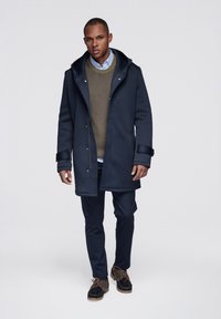 Navy blue wool blend coat with a large hood, snap closures, and side pockets, layered over a green knit sweater and light blue shirt.