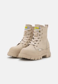 Stivali alla caviglia beige con suola platform spessa, realizzati in suede, con un design con lacci e un'asola sul retro. Dettaglio etichetta gialla.