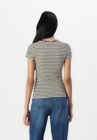 Rutet t-skjorte med korte ermer i beige og svart, tettsittende design med rund hals, kombinert med løse blå denimjeans.