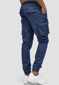 Joggers cargo azul marino con puños elásticos en los tobillos, bolsillos laterales distintivos y una tela texturizada, combinados con zapatillas deportivas blancas.