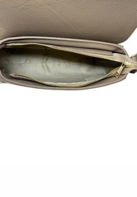Borsa a tracolla in pelle beige aperta per mostrare il vano principale vuoto con una cerniera dorata e una fodera di tessuto chiaro.