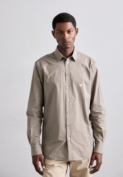 Chemise à boutons marron et tan à motif vichy, avec des manches longues et un col écarté. Présente des boutons blancs et un petit logo sur la poitrine.