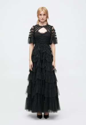 Schwarzes, gestuftes Maxikleid aus Tüll mit Rüschendetails, durchsichtigen kurzen Ärmeln und einem Schlüsselloch-Ausschnitt. Abgeschlossen mit einem figurbetonten Oberteil.