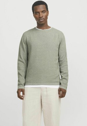 Suéter de punto verde claro con cuello redondo, patrón texturizado, mangas largas y un cuello interior blanco de contraste, combinado con pantalones claros.