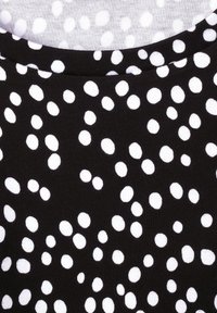 Černá látka s různými bílými puntíky; hladká textura s některými puntíky, které se zdají být mírně rozmazané, což vytváří kontrast a vizuální zajímavost.