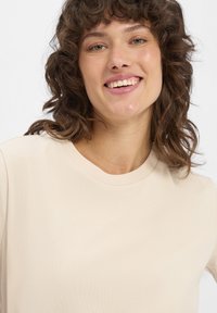 Beige Rundhals-T-Shirt aus weichem Stoff; kurze Ärmel und glatte Textur. Einfaches Design ohne Muster oder sichtbare Hardwaredetails.