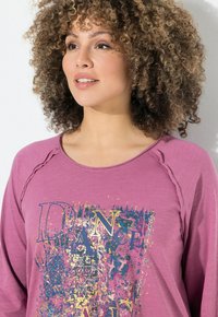 Camisetta a maniche lunghe viola con stampa grafica che presenta la parola "DANCE" in giallo e blu, tessuto texturizzato e maniche raglan.